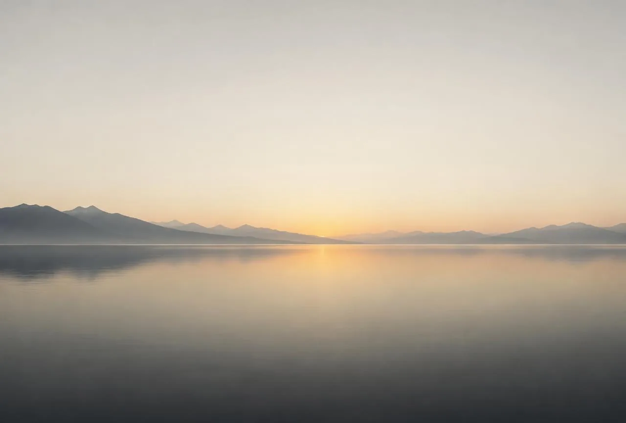 A calm horizon over still water at dawn, with distant alpine silhouettes
